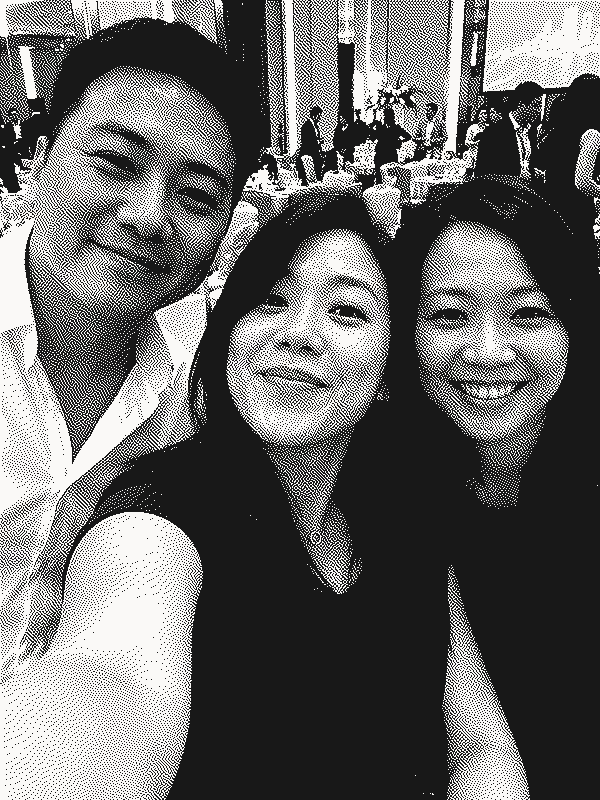 Three colleagues taking a smiling selfie together at a company dinner, shown as a grainy black-and-white print.